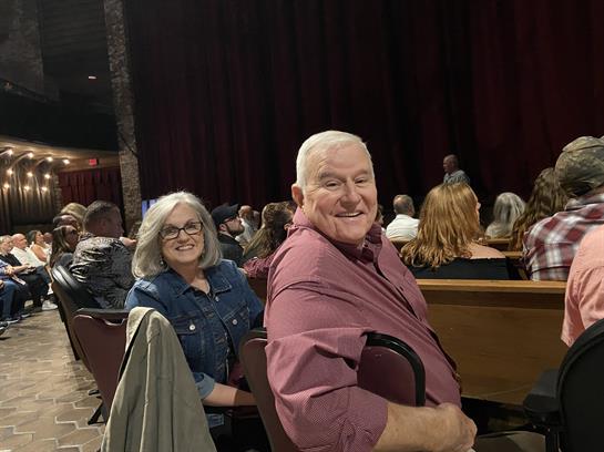 Couple smiles while seated in a crowded theater, engaged in a lively live performance.