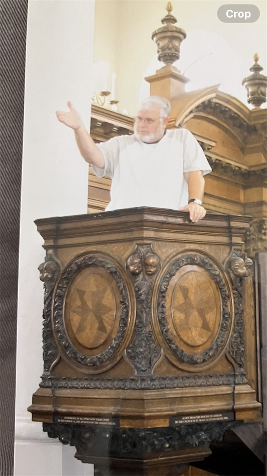An elderly man stands at a wooden pulpit, passionately speaking in a historic church setting.