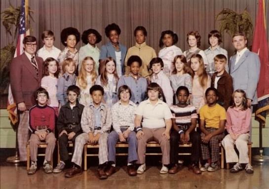 Twenty-five students and two adult teachers pose together in a classroom setting from the 1970s.