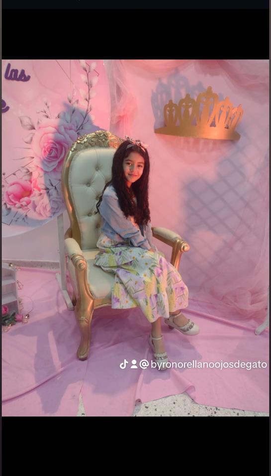 A young girl poses gracefully in a floral dress on a luxurious chair amidst vibrant decorations.
