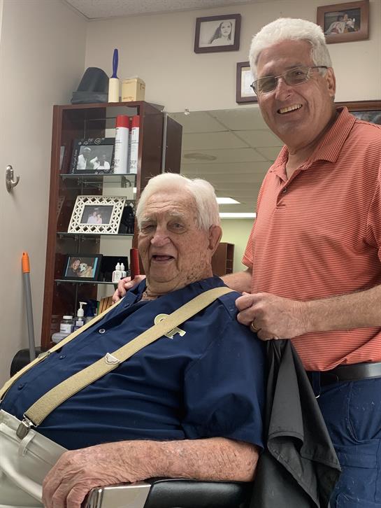 Barber gives haircut to older man, both smiling in a vibrant barbershop filled with memories.