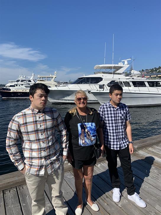 Group of three stands by the water, enjoying a sunny day near luxurious yachts.