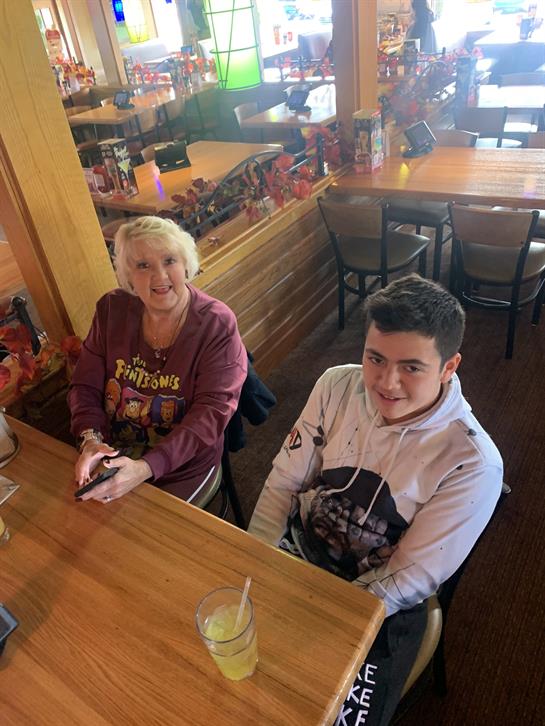 A woman and a young man sit at a wooden table in a busy restaurant, enjoying each other's company.