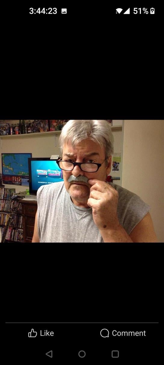 An elderly man with gray hair and glasses appears deep in thought while at home.