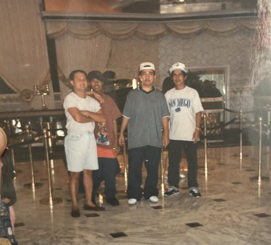 Four friends stand together, smiling, in a spacious indoor area with modern decor.