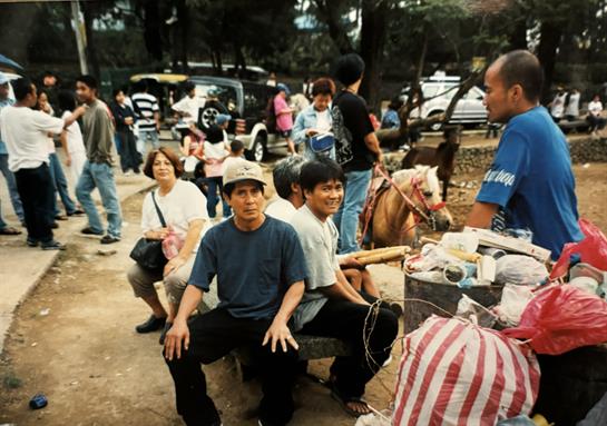 Individuals gather around a local market, enjoying food, horse rides, and socializing in a park.