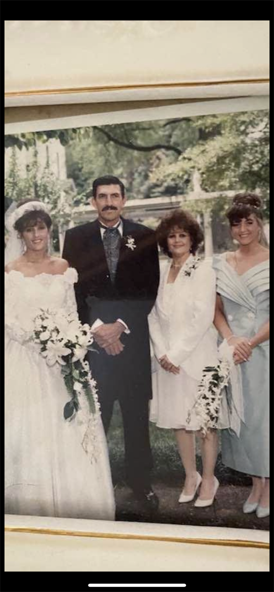 A bride and her family pose together at a sunny outdoor wedding reception amid flowers.