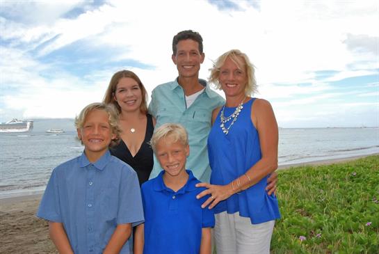A joyful family poses together by the beach, enjoying the beautiful weather and ocean view.