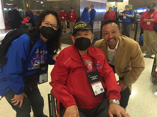 Two people pose with an elderly veteran in a wheelchair at an airport honoring his service.
