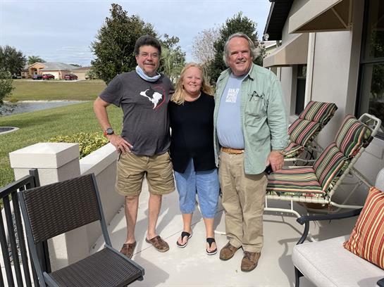 Three friends embrace each other with smiles while enjoying a sunny outdoor gathering.