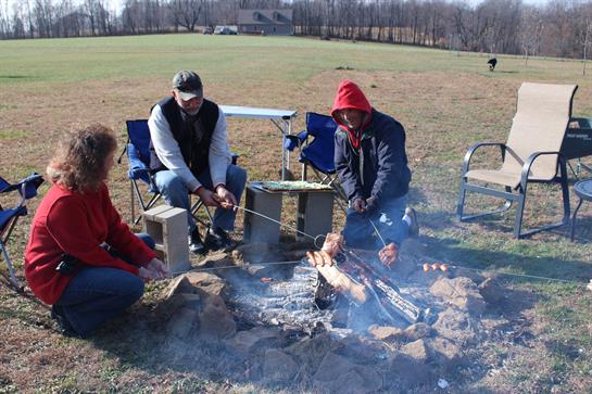 Friends enjoy a cozy campfire experience while roasting food in a peaceful, open field.