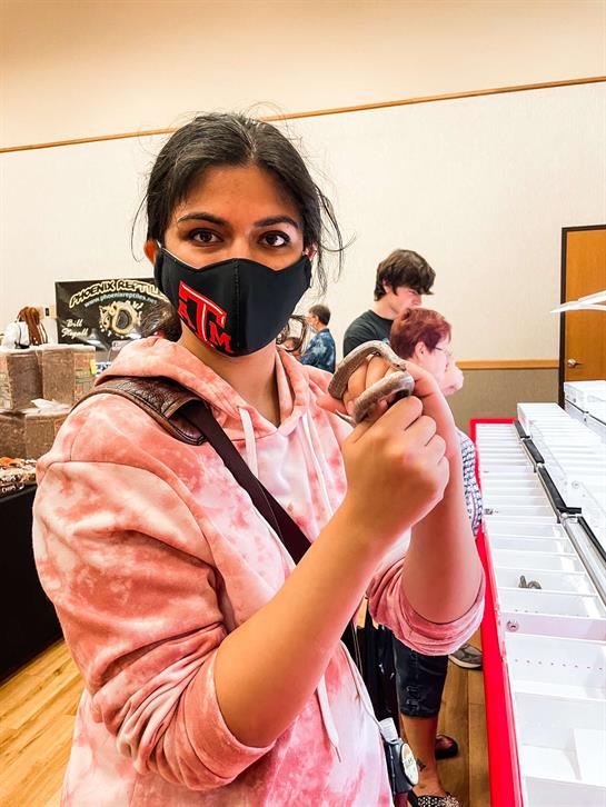 A young woman with a mask carefully handles a small snake during a lively event in a community hall.