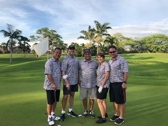 Friends celebrate a day of golf under a blue sky with palm trees surrounding the green.