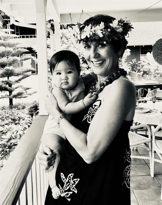 A woman in a dress welcomes the day while holding a baby adorned with a charming expression.