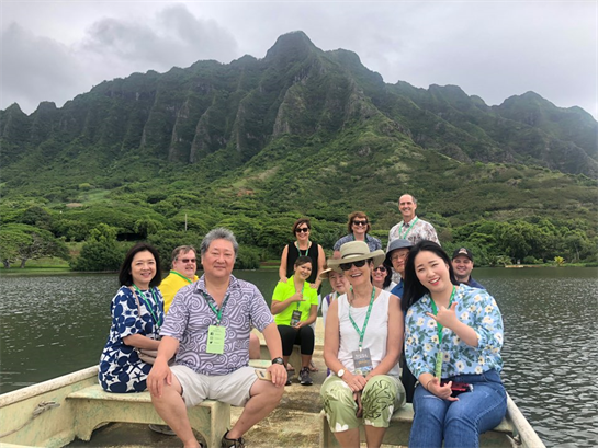 Tourists relax on a boat while surrounded by lush mountains and cloudy skies in Hawaii.