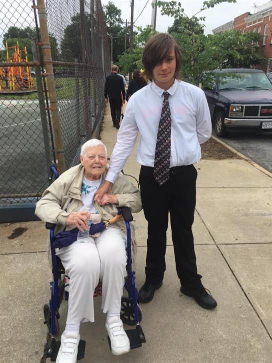A man standing next to an old woman in a wheelchair