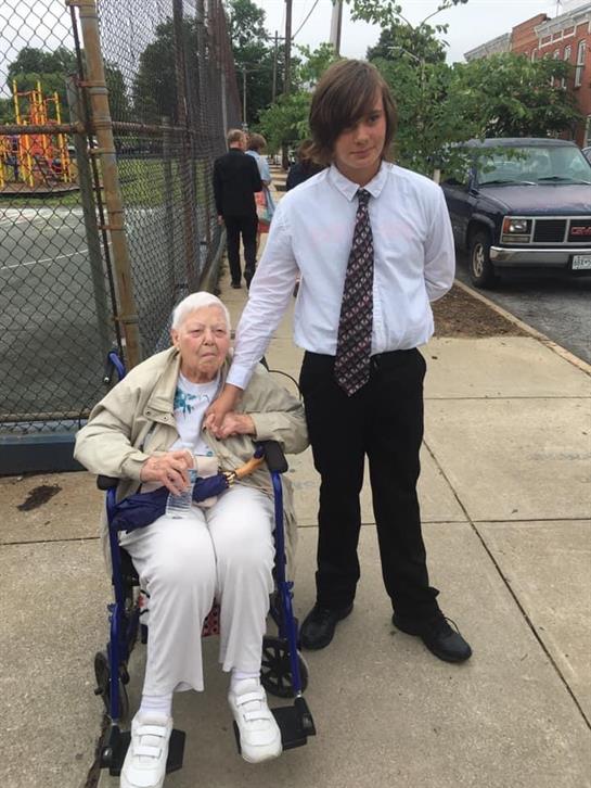 A young man standing next to an old woman in a wheelchair