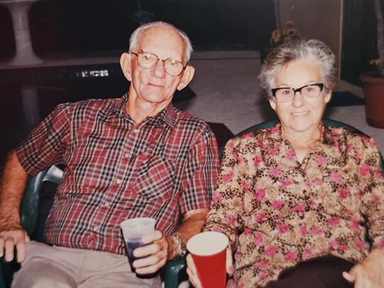 An elderly couple shares a warm moment while holding drinks in a cozy indoor setting.