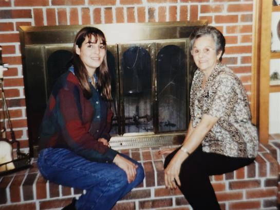 Two women sit on a brick hearth, smiling warmly while spending time together indoors.