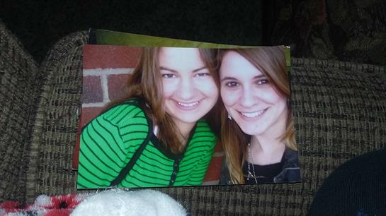 Two friends pose happily in front of a brick wall, showcasing joyful expressions and a casual vibe.