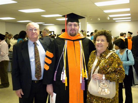 Graduate poses proudly with parents after receiving their degree in a crowded hall.