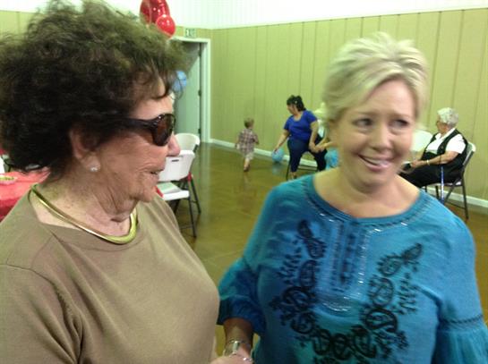 Women talk joyfully together while others enjoy activities in a community center.