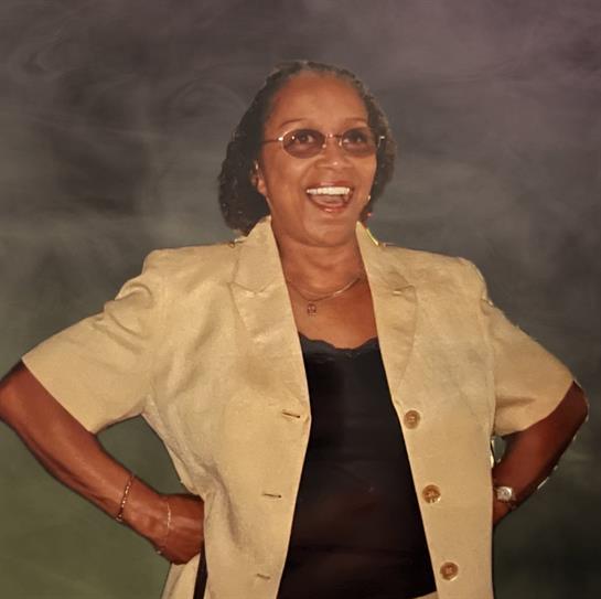 A joyful woman stands confidently with hands on her hips, exuding happiness in a studio environment.