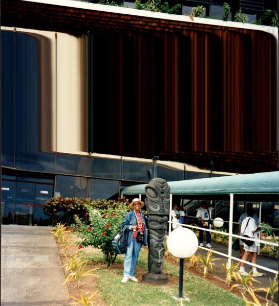 People gather near a vibrant building adorned with a totem pole, amidst tropical flora.
