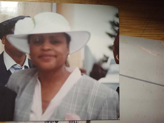 A woman in a stylish white hat smiles while standing beside a gentleman at a festive gathering.