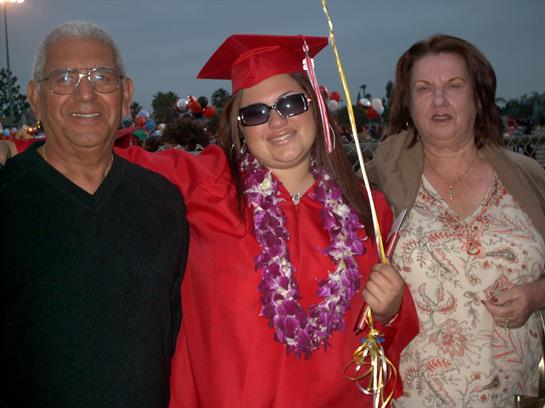 Family celebrates graduation together during an outdoor ceremony at sunset.