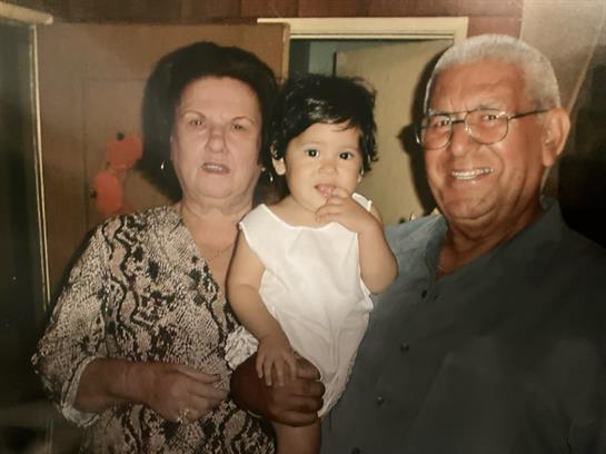 Grandparents pose proudly with their young grandchild in a cozy home environment.