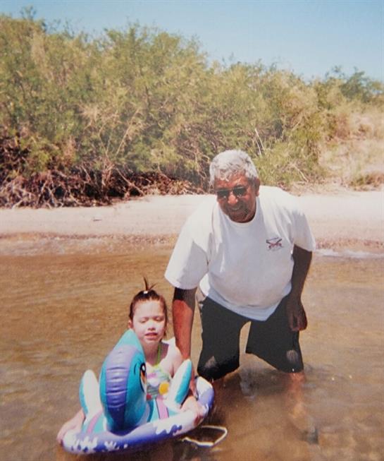 A grandparent and a child are playing by the river, enjoying the warm sun and gentle water.