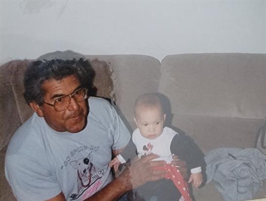 A grandfather lovingly holds his grandchild on a couch in a comfortable home setting.
