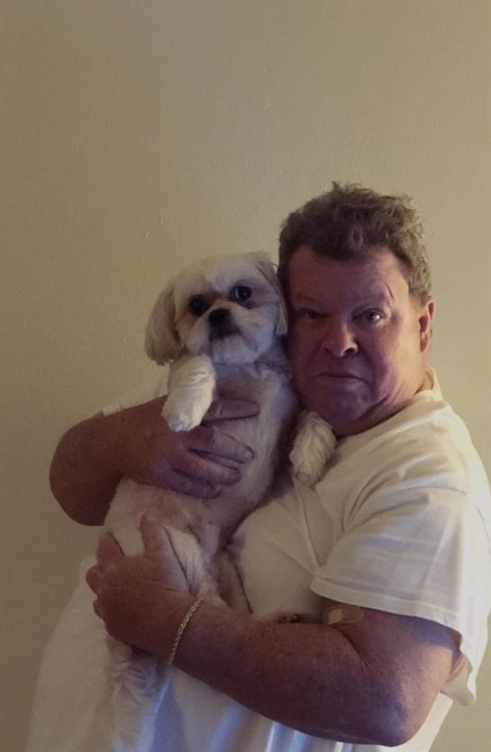 A man gently cradles a small dog against his chest in a warm and intimate indoor atmosphere.