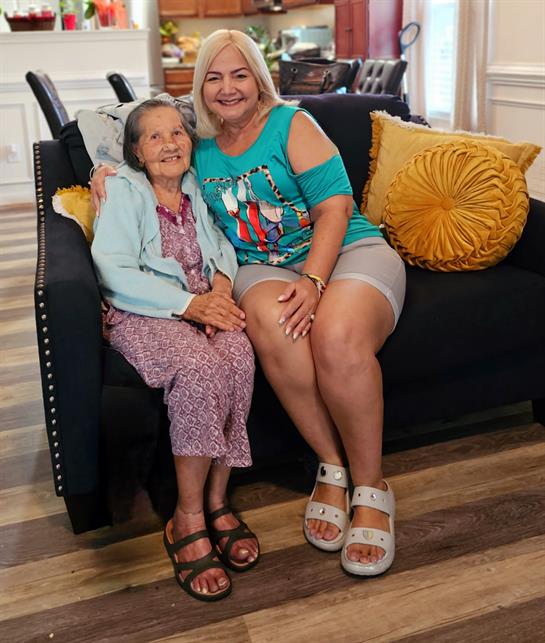 Two women smile on a comfy sofa, enjoying each other's company in a cozy setting.