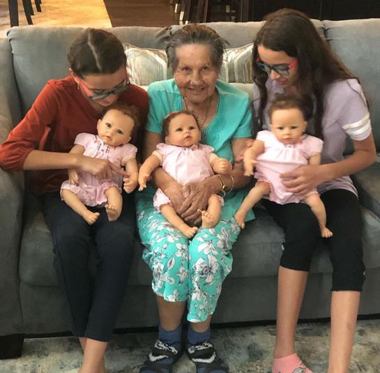 Three girls and their grandmother sit comfortably together, each with a doll.