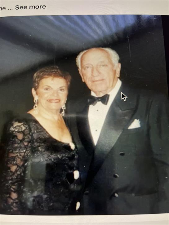 A couple smiles together at a formal gathering, wearing elegant attire and enjoying the moment.