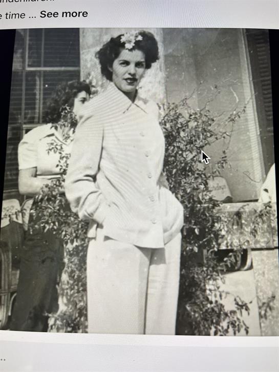 Elegant woman sports vintage attire while posing in a garden with greenery around her.