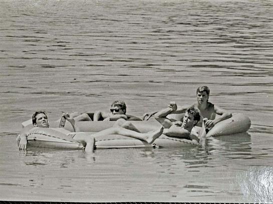 Friends enjoy leisure time on inflatable rafts in a peaceful lake under clear summer skies.