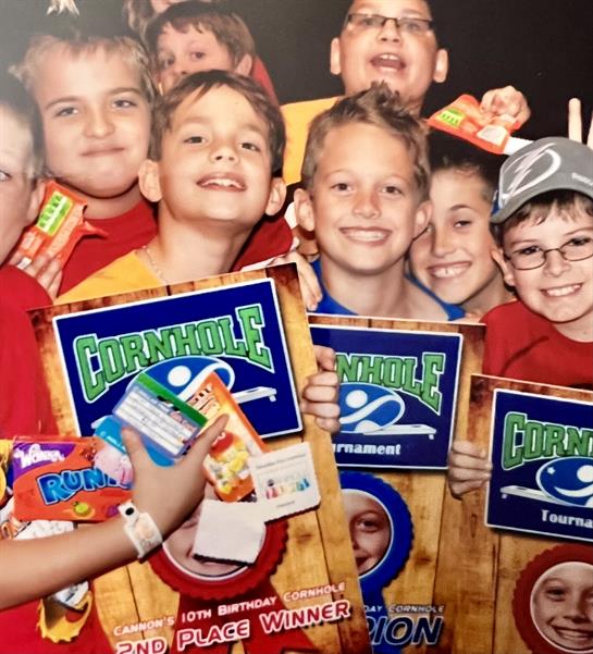 Children hold awards and snacks, excited after competing in a cornhole tournament.