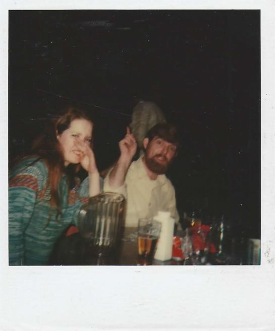 Two friends share a moment of joy at a nighttime gathering, surrounded by drinks and chatter.
