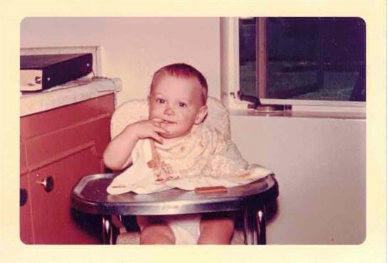 A cheerful baby enjoys a snack while seated in a high chair, bathed in soft sunlight.