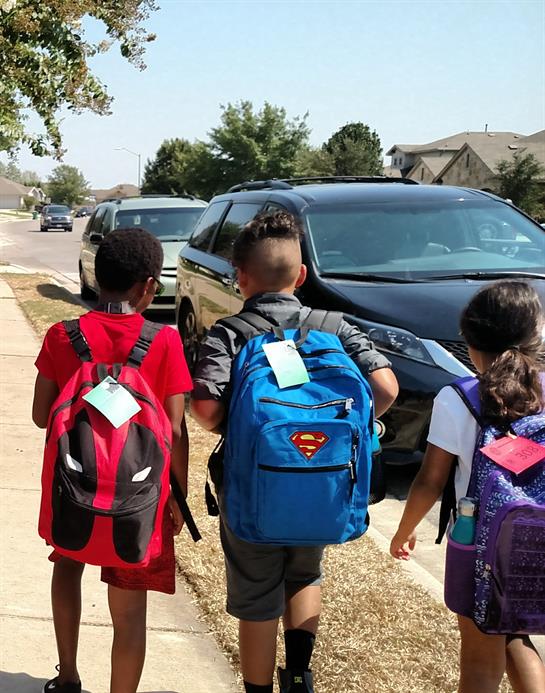A group of kids walking on the sidewalk with backpacks