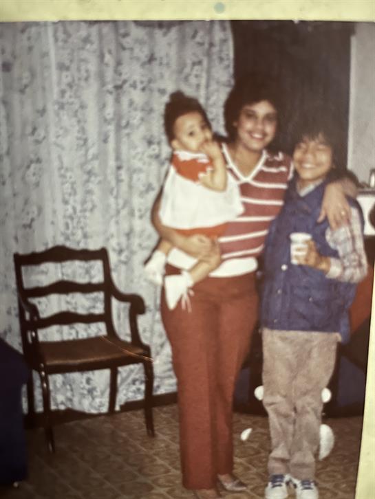 A mother holds a baby while two children smile joyfully in a warmly decorated living room.