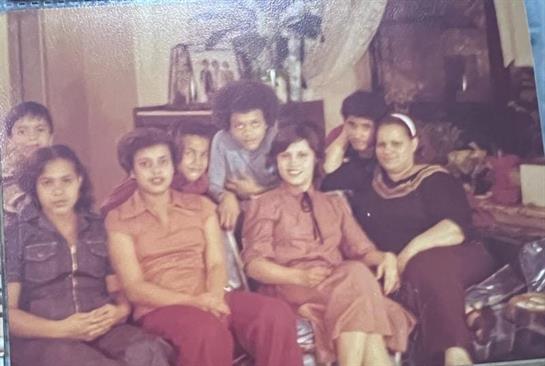 A group of eight family members poses together in a warm living room, smiling happily.