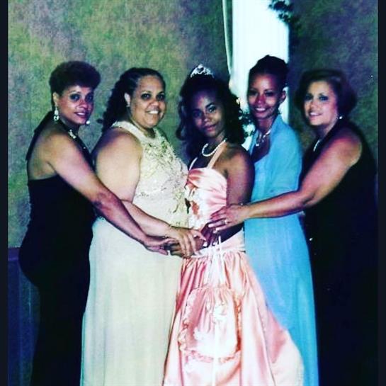 Five women dressed in colorful gowns gather together, smiling and celebrating a memorable occasion.
