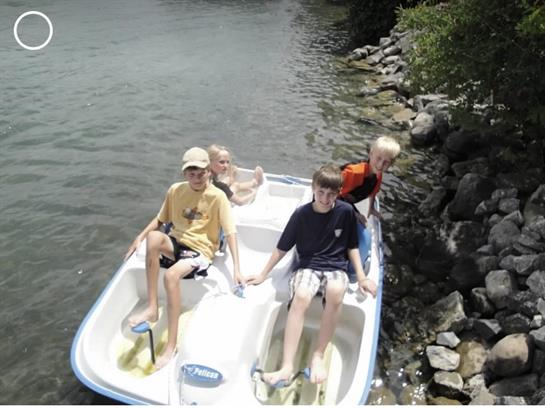 Four children are having fun pedaling a boat in a serene lake surrounded by rocks.