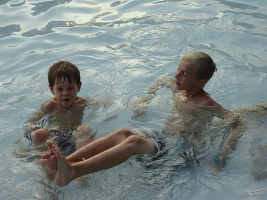 Two young boys splash and play joyfully in clear water under the warm sun.