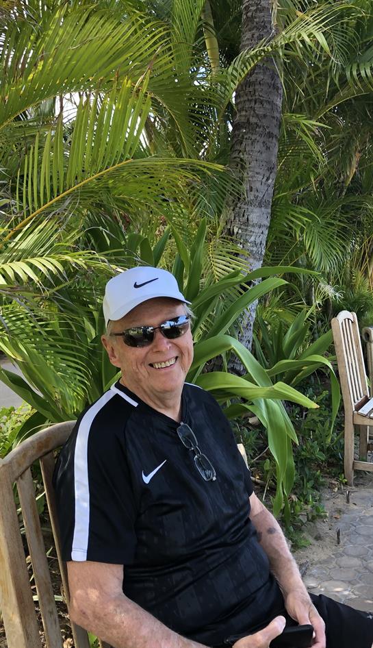 Senior man seated in tropical garden, enjoying sunshine and surrounded by lush plants.
