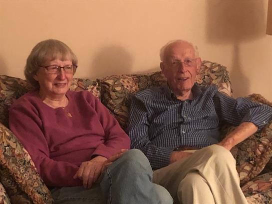 Senior couple relaxes on a patterned couch, sharing joyful moments in their cozy living room.